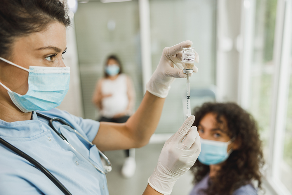 Nurse holding syringe and making Covid-19 vaccination injection dose in shoulder of patient.