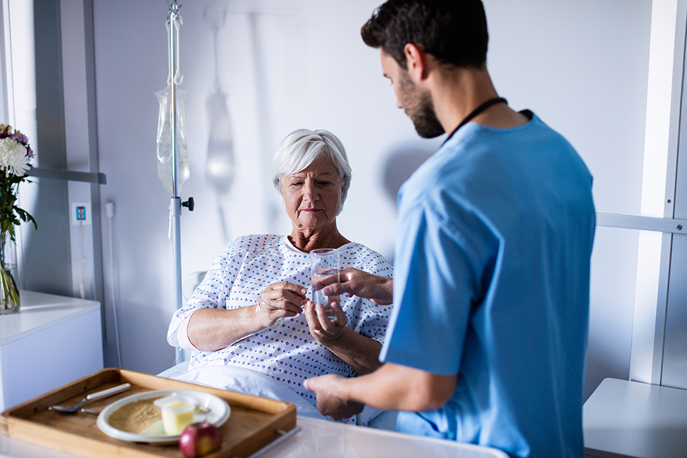 Doctor serving medicine to female senior patient on bed in hospital